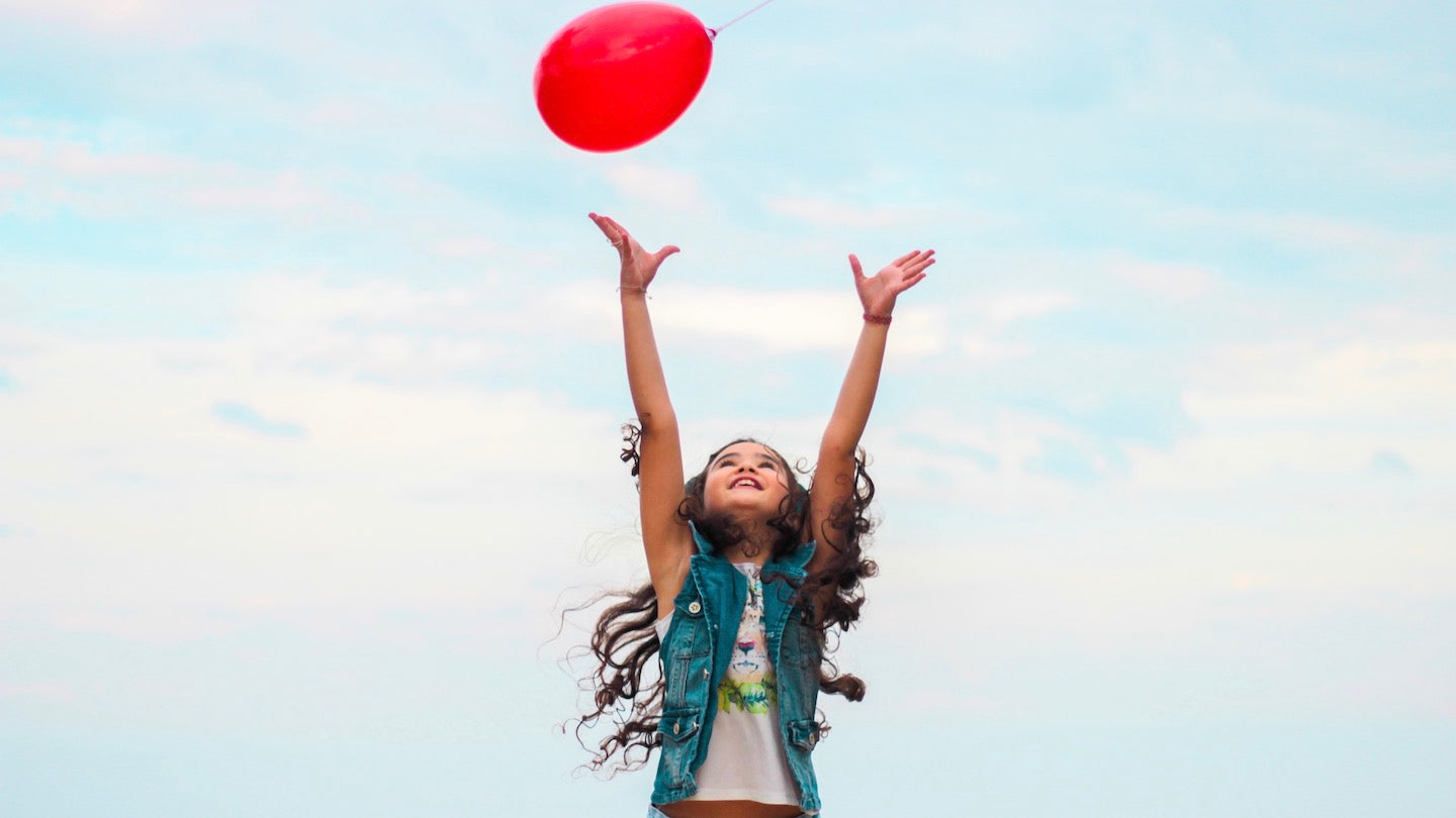 Petite fille lance un ballon rouge vers le ciel