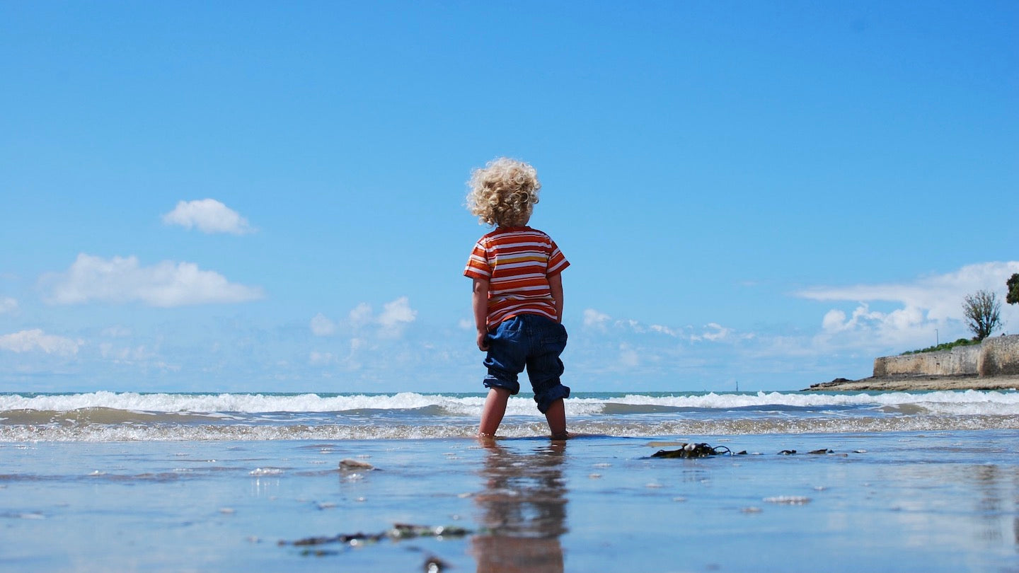 Petit garçon aux cheveux blonds à la mer qui regarde l'horizon
